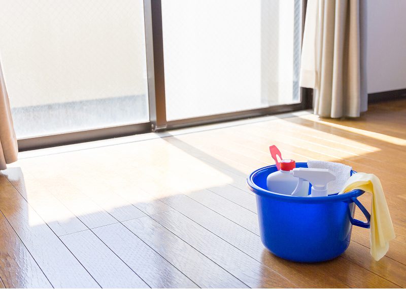 Blue bucket filled with cleaning supplies on a wooden floor.