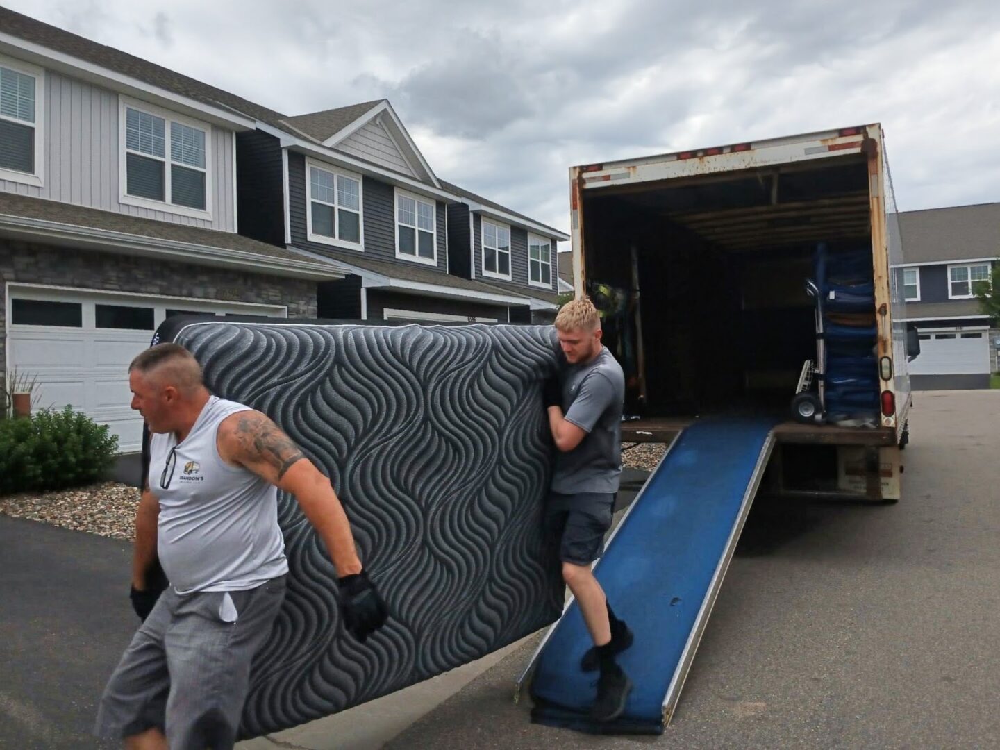 Two movers carrying a mattress into a residence.